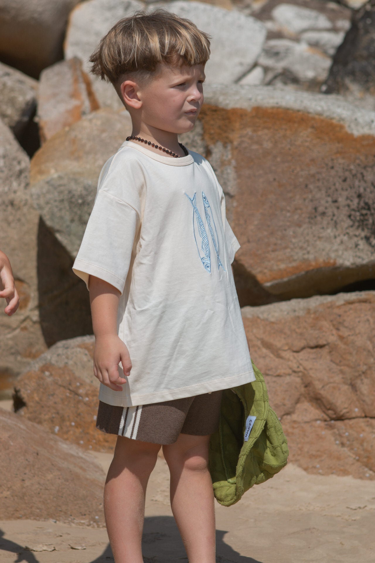 Child standing on a rocky surface wearing a white t-shirt and brown shorts.
